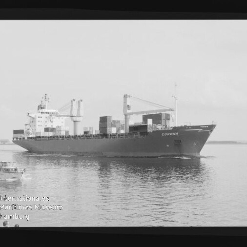 Schwarzweiß-Foto eines Containerschiffs mit der Aufschrift CORONA, beladen mit Containern und zwei Deckskränen, das auf ruhigem Wasser fährt; links im Vordergrund ein kleines Beiboot und am Bildrand ein Filmstreifen mit Museumsstempel sichtbar.