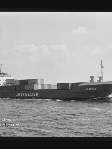 Schwarzweiß-Seitenansicht eines Containerschiffs mit der Beschriftung UNIFEEDER und dem Namen Coronel auf dem Bug, beladen mit Containern und fahrend auf ruhiger See unter leicht bewölktem Himmel; Museumslogo unten links.