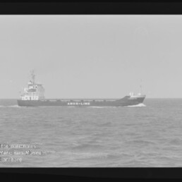 Schwarz-weiß-Foto eines Frachtschiffs mit der Aufschrift AROS-LINE, das auf leicht welliger See fährt; Filmrand sichtbar und Wasserzeichen des Internationalen Maritimen Museums Hamburg unten links.
