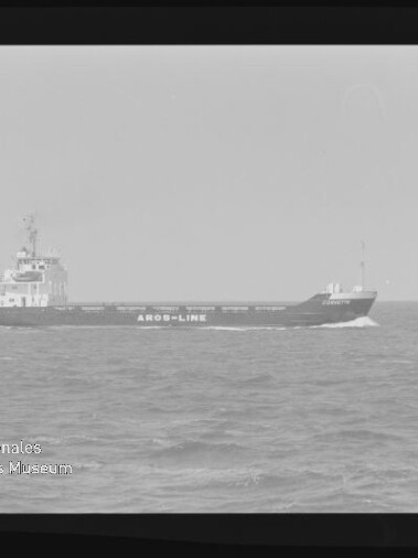 Schwarz-weiß-Foto eines Frachtschiffs mit der Aufschrift AROS-LINE, das auf leicht welliger See fährt; Filmrand sichtbar und Wasserzeichen des Internationalen Maritimen Museums Hamburg unten links.