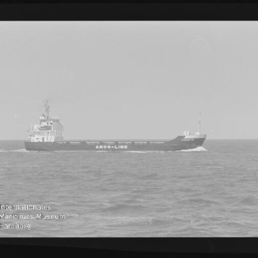 Schwarz-weiß-Foto eines Frachtschiffs mit der Aufschrift AROS-LINE, das auf leicht welliger See fährt; Filmrand sichtbar und Wasserzeichen des Internationalen Maritimen Museums Hamburg unten links.