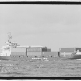 Schwarzweiß-Foto eines Containerschiffs der Aros-Line mit gestapelten Containern und dem Namen 'Corvette' am Bug, auf See bei leichtem Seegang, mit sichtbarem Wasserzeichen des Internationalen Maritimen Museums Hamburg.