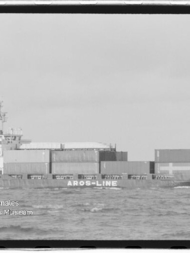 Schwarzweiß-Foto eines Containerschiffs der Aros-Line mit gestapelten Containern und dem Namen 'Corvette' am Bug, auf See bei leichtem Seegang, mit sichtbarem Wasserzeichen des Internationalen Maritimen Museums Hamburg.