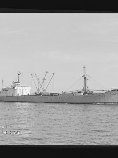Schwarzweiß-Foto einer Frachtschiff-Seitenansicht auf ruhiger See mit sichtbaren Ladekränen und Masten, rechteckigem Filmrand und Museumslogo in der unteren linken Ecke.