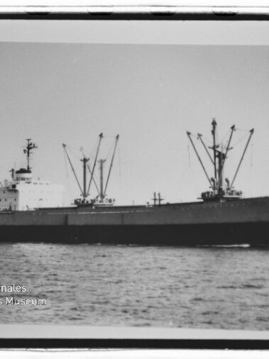 Schwarz-weiß-Foto eines Frachters in Seitenansicht auf ruhiger See mit mehreren Ladekränen auf dem Deck und dem Wasserzeichen des Internationalen Maritimen Museums Hamburg in der unteren linken Ecke.