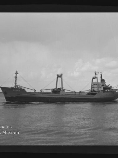 Schwarzweiß-Foto eines Frachtschiffs in Seitenansicht mit Ladekränen und Aufbau, das ruhig auf dem Meer vor niedrigem Horizont fährt; links unten Logo des Internationalen Maritimen Museums Hamburg.