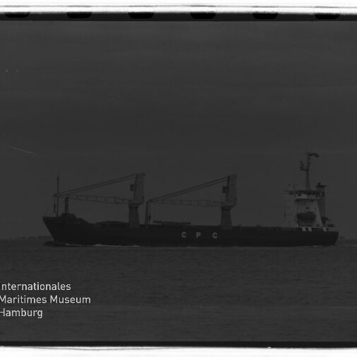 Schwarz-weiße Aufnahme eines Frachtschiffs mit zwei Deckskränen und den Buchstaben «C P C» am Rumpf, das auf ruhiger See vor dem Horizont fährt; unten links sichtbares Logo und Schriftzug des Internationalen Maritimen Museums Hamburg.