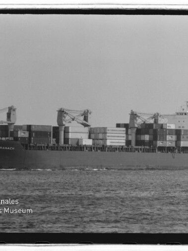 Containerschiff 'CRANACH' auf ruhiger See, beladen mit gestapelten Containern und drei Deckskränen; Schwarzweißaufnahme mit Museumswasserzeichen unten links.