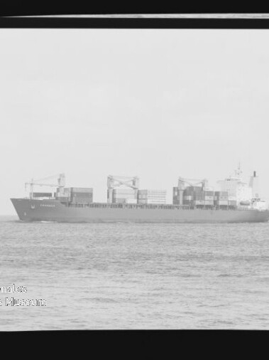 Schwarzweißaufnahme eines containerbeladenen Frachtschiffs in Seitenansicht auf ruhiger See, mit Ladekränen und gestapelten Containern, sichtbaren Filmrändern und Wasserzeichen des Internationalen Maritimen Museums Hamburg.