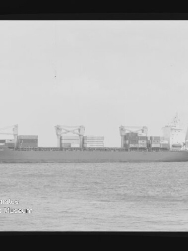 Schwarzweiß-Seitenansicht eines Containerschiffs mit aufgestapelten Containern und drei großen Deckskranen auf ruhiger See, mit schwarzem Filmrand und Museumslogo unten links