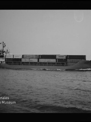 Schwarzweiß-Profilaufnahme eines Containerschiffs mit übereinander gestapelten Ladecontainern, das zügig über das Meer fährt; unten links das Logo des Internationalen Maritimen Museums Hamburg.