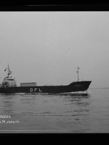 Schwarzweiß-Foto eines mittleren Frachtschiffs mit großen weißen Buchstaben „DFL“ am Rumpf, das ruhig auf ruhiger See fährt; unten links das Logo des Internationalen Maritimen Museums Hamburg und am rechten Bildrand die Beschriftung „AGFA LISS“.