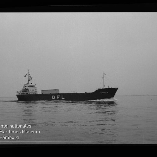 Schwarzweiß-Foto eines mittleren Frachtschiffs mit großen weißen Buchstaben „DFL“ am Rumpf, das ruhig auf ruhiger See fährt; unten links das Logo des Internationalen Maritimen Museums Hamburg und am rechten Bildrand die Beschriftung „AGFA LISS“.