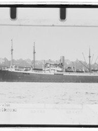 Schwarzweißaufnahme eines langen Dampfschiffs in Seitenansicht mit mehreren Masten und einem Schornstein, das auf ruhigem Wasser vor einer Uferbebauung liegt; umgeben von Negativrand und Museumsstempel.