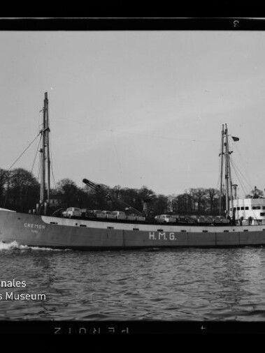 Schwarzweiß-Foto eines zweimastigen Frachtschiffs (Name 'CREMON') mit großer Aufschrift 'H.M.G.' am Rumpf, das mit Bugwelle auf ruhiger See vor einer baumbestandenen Küstenlinie fährt; links unten das Logo des Internationalen Maritimen Museums Hamburg.