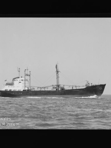 Schwarzweißaufnahme eines Frachtschiffs mit Mittschiffsaufbau und Ladekranen, das in ruhiger See fährt; am Bildrand sind der Filmrahmen mit der Aufschrift PERUTZ und ein Museumswasserzeichen unten links sichtbar.