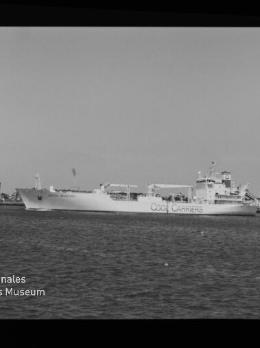 Schwarzweißaufnahme eines großen Frachtschiffs mit der Aufschrift COOL CARRIERS im Hafen, im Vordergrund Wasser, am Bildrand Filmmarkierung AGFA APX 100 und Museumslogo unten links.