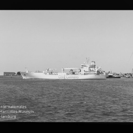 Schwarzweiß-Foto eines Frachtschiffs mit der Aufschrift „Cool Carriers“, das auf ruhigem Wasser in einem Hafen vor Küstenbebauung liegt; Filmrand und Wasserzeichen des Internationalen Maritimen Museums Hamburg sind sichtbar.