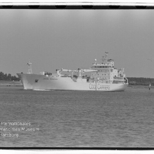 Schwarzweiß-Foto eines großen Kühlschiffs mit der Aufschrift „COOL CARRIERS“, das ruhig auf dem Wasser vor einer flachen Baumküste fährt; sichtbare Filmränder und Museumswasserzeichen im Bild.
