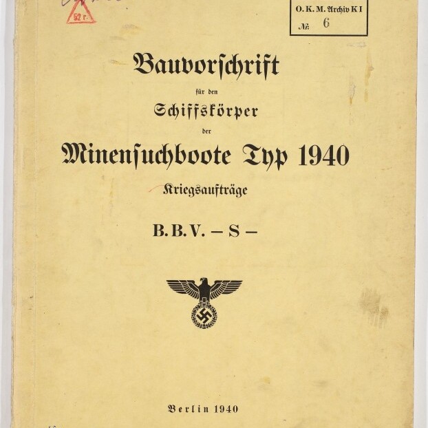 Vergilbtes Deckblatt einer Bauvorschrift von 1940 für Minensuchboote, mit schwarzer Frakturschrift, einem Reichsadler mit Hakenkreuz in der Mitte sowie Stempeln, handschriftlichen Vermerken und der Ortsangabe ‚Berlin 1940‘.