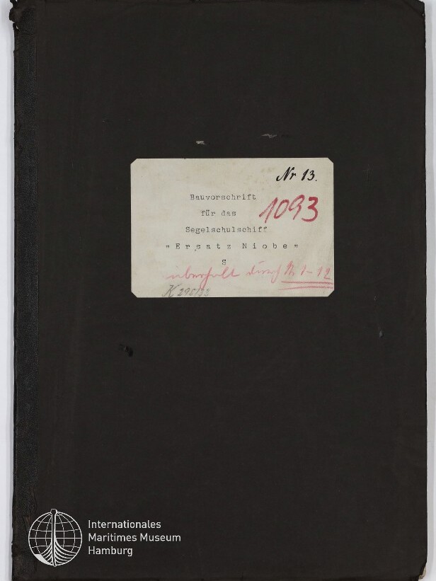Schwarzer Einband eines Akten- oder Buchumschlags mit mittig befestigtem weißem Etikett, auf dem handschriftlich ‚Nr. 13‘ und in Rot ‚1093‘ sowie getippt ‚Bauvorschrift für das Segelschulschiff „Ersatz Niobe“‘ stehen; unten links das Logo des Internationalen Maritimen Museums Hamburg.