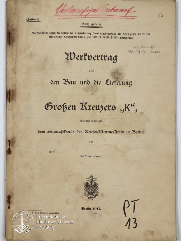 Deckblatt eines historischen Vertrags mit dem großen Titel „Werkvertrag über den Bau und die Lieferung des Großen Kreuzers ‚K‘“, oben handschriftlich in Rot „Vorentwurf“, gedruckt „Berlin 1911“ und ein preußischer Adler als Wappen, seitliche Rost- und Wasserflecken am Einband sowie Museumslogo unten links und handschriftliche Notiz „PT 13“ unten rechts.