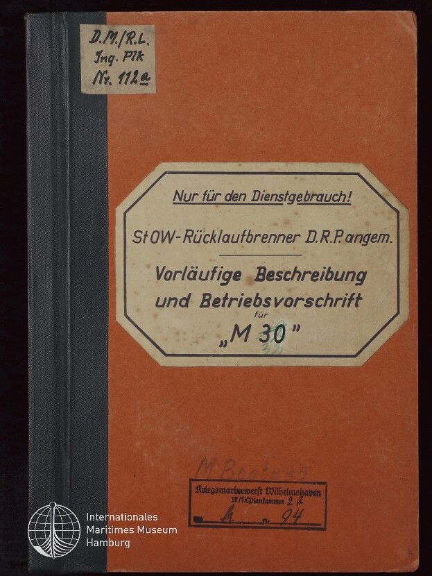 Orangener Einband eines technischen Handbuchs mit schwarzem Rücken; großes achteckiges Etikett mittig mit dem gedruckten Hinweis „Nur für den Dienstgebrauch!“ und dem Titel „Vorläufige Beschreibung und Betriebsvorschrift für ‚M 30‘“, oben links ein handschriftlicher Zettel sowie unten ein Stempel der Kriegsmarinewerft Wilhelmshaven und das Logo des Internationalen Maritimen Museums Hamburg.