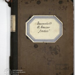 Buchdeckel eines alten braunen Notizbuchs mit schwarzem Leineneinband und ausgefransten Ecken; mittig ein achteckiges Etikett mit handschriftlicher Aufschrift „Bauvorschrift Kl. Kreuzer ‚Emden‘“, handschriftliche Nummer 638 oben rechts, Wasserflecken und ein Stempel sowie Museumssiegel unten links.