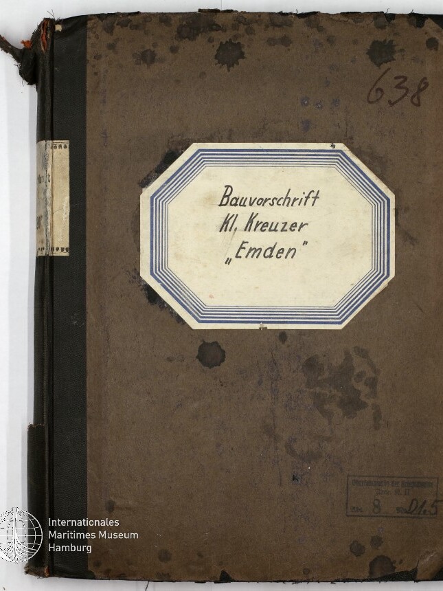 Buchdeckel eines alten braunen Notizbuchs mit schwarzem Leineneinband und ausgefransten Ecken; mittig ein achteckiges Etikett mit handschriftlicher Aufschrift „Bauvorschrift Kl. Kreuzer ‚Emden‘“, handschriftliche Nummer 638 oben rechts, Wasserflecken und ein Stempel sowie Museumssiegel unten links.