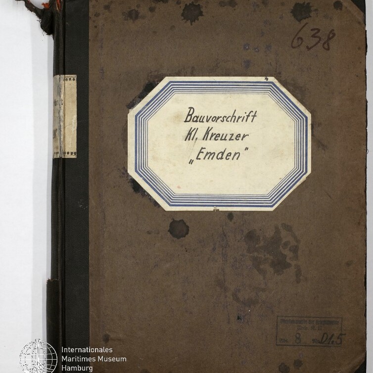 Buchdeckel eines alten braunen Notizbuchs mit schwarzem Leineneinband und ausgefransten Ecken; mittig ein achteckiges Etikett mit handschriftlicher Aufschrift „Bauvorschrift Kl. Kreuzer ‚Emden‘“, handschriftliche Nummer 638 oben rechts, Wasserflecken und ein Stempel sowie Museumssiegel unten links.