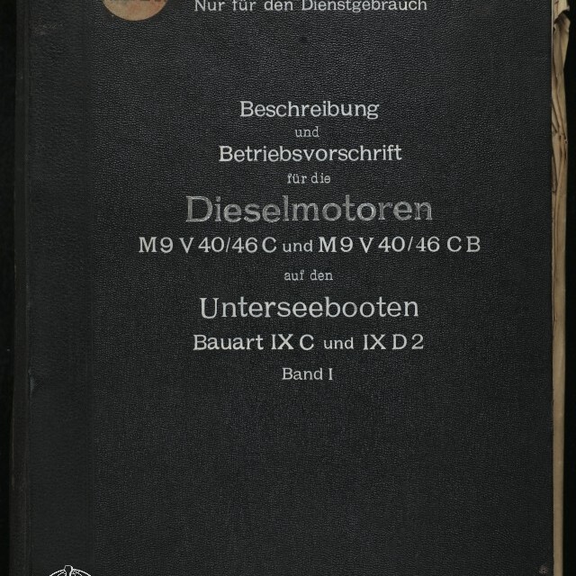 Schwarzer, leicht abgenutzter Bucheinband mit weißer deutscher Aufschrift über Dieselmotoren für Unterseeboote (M9 V 40/46 C und M9 V 40/46 C B), rundem Aufkleber oben links und Logo des Internationalen Maritimen Museums Hamburg unten links.