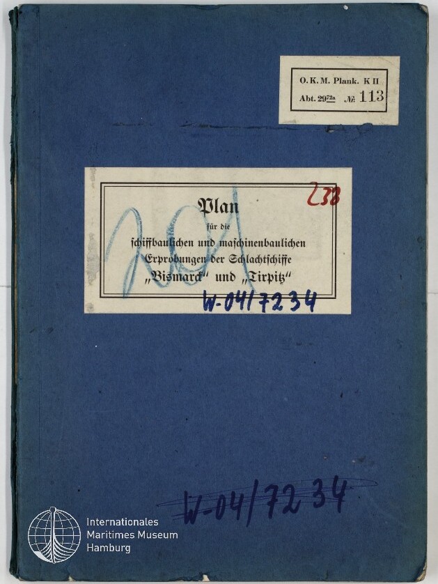 Blauer, leicht abgenutzter Ordnerumschlag mit zwei weißen Aufkleberetiketten — oben rechts ein kleines Etikett mit der Beschriftung O.K.M. Plank. K II Abt. 2972 Nr. 113, mittig ein größeres Etikett mit dem gedruckten Titel zu den Schlachtschiffen Bismarck und Tirpitz sowie handschriftlichen Nummern in Blau und Rot, unten links das Logo des Internationalen Maritimen Museums Hamburg.