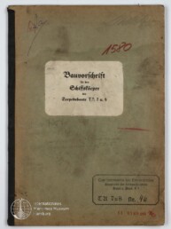 Verschmutzter grüner Einband eines alten technischen Hefts mit mittig aufgeklebtem weißen Etikett mit dem Titel Bauvorschrift für den Schiffskörper der Torpedoboote T5, 7 u. 8, roten Stempeln und Museumswasserzeichen unten links