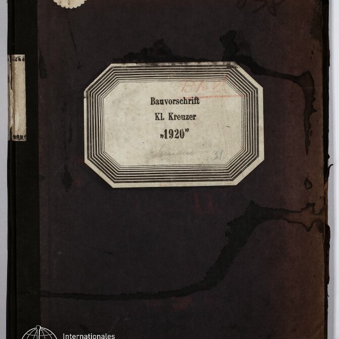 Verwittertes dunkelbraunes Buch- bzw. Ordnercover mit oktogonalem Etikett in der Mitte, auf dem »Bauvorschrift Kl. Kreuzer „1920”« steht; sichtbare Wasserflecken, handschriftliche Zahl »638« oben rechts, runder Aufkleber oben links und Museumslogo unten links.