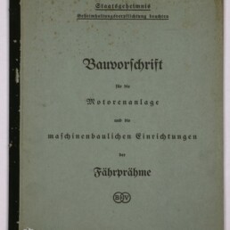 Deckblatt eines alten hellgrün-blauen Heftes mit schwarzem Leinenrücken; oben Stempel ‚Staatsgeheimnis‘ und ‚Geheimhaltungsverpflichtung beachten‘, mittig in Frakturschrift der Titel ‚Bauvorschrift für die Motorenanlage und die maschinenbaulichen Einrichtungen der Fähpräme‘ mit rundem B&V-Emblem darunter, das Papier zeigt braune Stockflecken; unten links Logo des Internationalen Maritimen Museums Hamburg und unten rechts handschriftliche Kennzeichnung ‚319 D‘.