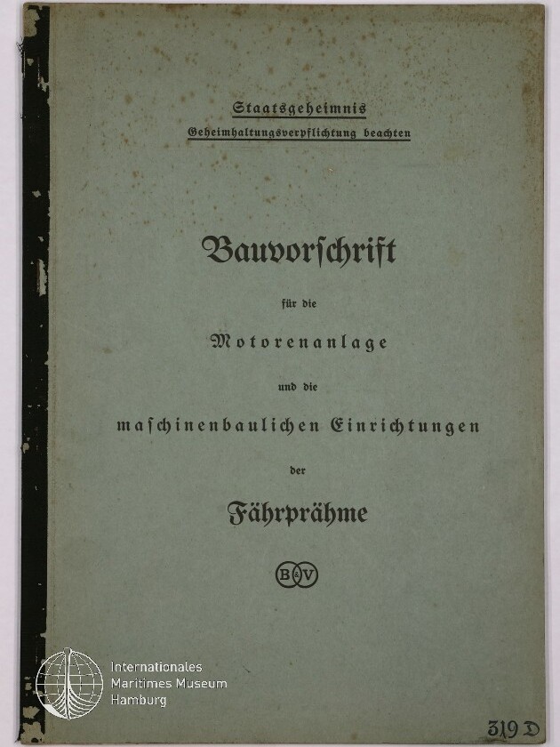 Deckblatt eines alten hellgrün-blauen Heftes mit schwarzem Leinenrücken; oben Stempel ‚Staatsgeheimnis‘ und ‚Geheimhaltungsverpflichtung beachten‘, mittig in Frakturschrift der Titel ‚Bauvorschrift für die Motorenanlage und die maschinenbaulichen Einrichtungen der Fähpräme‘ mit rundem B&V-Emblem darunter, das Papier zeigt braune Stockflecken; unten links Logo des Internationalen Maritimen Museums Hamburg und unten rechts handschriftliche Kennzeichnung ‚319 D‘.