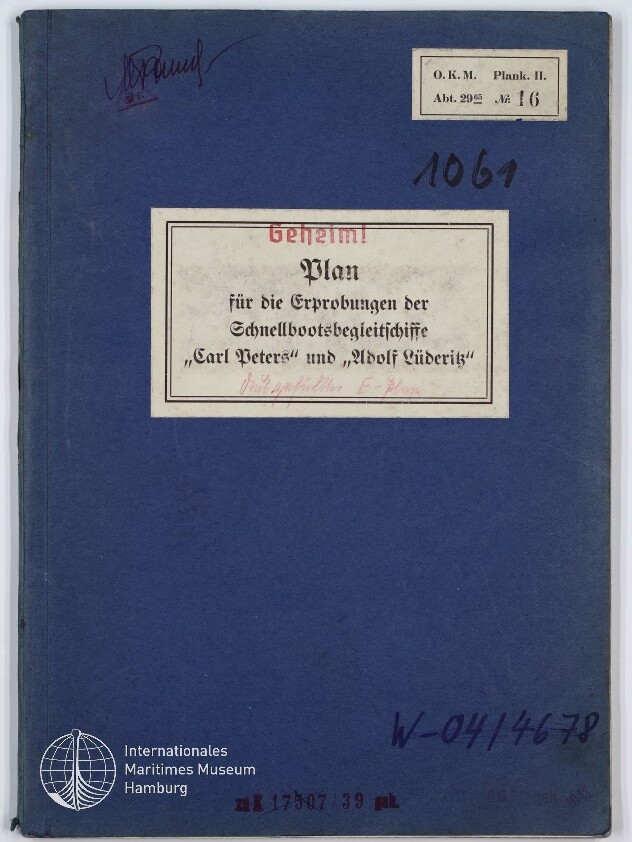 Blauer Einband eines historischen Hefts mit mittiger Etikette 'Geheim! Plan für die Erprobungen der Schnellbootsbegleitschiffe „Carl Peters“ und „Adolf Lüderitz“', handschriftlichen Nummern, Stempeln und einem Museumslogo in der unteren Ecke.
