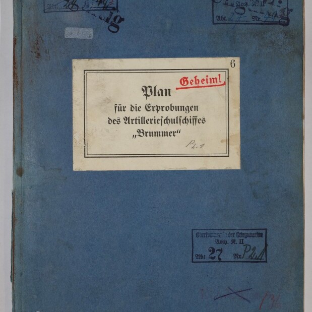 Blaues, altes Ordnerdeckblatt mit einem aufgeklebt weißen Etikett, auf dem in schwarzer Schrift und rot gestempelt „Geheim! Plan für die Erprobungen des Artillerieschulschiffes ‚Brummer‘“ steht; Umschlag zeigt mehrere Stempel, handschriftliche Notizen, Nummern, Gebrauchsspuren und ein Museumssignet unten links.