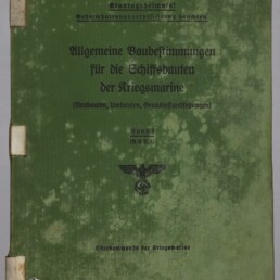 Grünes, stark vergilbtes und fleckiges Buchcover mit dem gedruckten Titel Allgemeine Baubestimmungen für die Schiffsbauten der Kriegsmarine, einem Reichsadler mit Hakenkreuz in der Mitte, handschriftlichen/stempelartigen Nummern oben links und dem Museumslogo Internationales Maritimes Museum Hamburg unten links