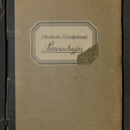 Abgenutztes braunes Heft mit schwarzem Buchrücken und sichtbaren Nahtfäden links, mittig ein etikettenartiges Schild mit der Handschrift 