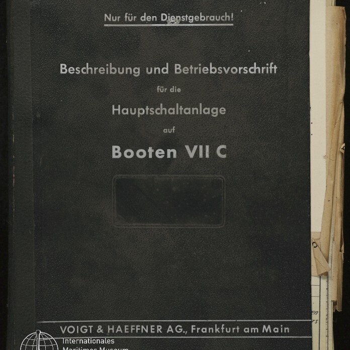 Schwarzer Ordnerumschlag mit weißer Aufschrift 'Nur für den Dienstgebrauch! Beschreibung und Betriebsvorschrift für die Hauptschaltanlage auf Booten VII C', Verlagszeile 'Voigt & Haeffner AG, Frankfurt am Main' und Museumssiegel unten links, an der rechten Seite herausragende Papiere.