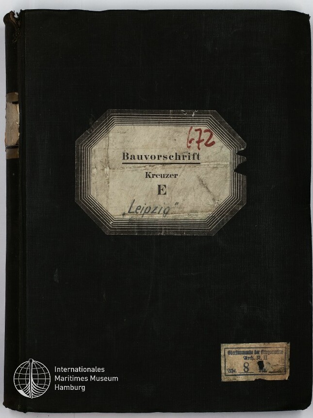 Schwarzer Leineneinband eines alten Buchs mit abgegriffenem Buchrücken, mittig aufgeklebt ein achteckiges, gealtertes Etikett mit der Aufschrift „Bauvorschrift Kreuzer E Leipzig“ und roter Ziffer ‚172‘, unten rechts ein kleines weiteres Etikett und links unten das Logo des Internationalen Maritimen Museums Hamburg.