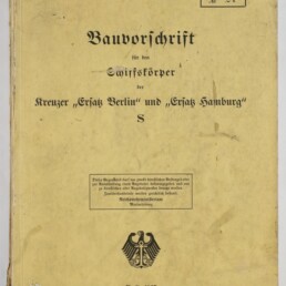Vergilbter Umschlag einer Bauvorschrift aus Berlin 1935 mit schwarzer Frakturschrift ‚Bauvorschrift für den Schiffskörper der Kreuzer „Ersatz Berlin“ und „Ersatz Hamburg“ S‘, schwarzem Reichsadler-Emblem, gestempelten Kästchen und Nummern sowie einer roten handschriftlichen „600“ oben rechts und sichtbaren Gebrauchsspuren am Rand.