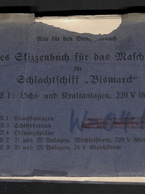 Abgewetztes blaues Heft mit deutschem Titel „Vorläufiges Skizzenbuch für das Maschinenpersonal für Schlachtschiff ‚Bismarck‘ — Band C1: Licht- und Kraftanlagen, 220 V Gleichstrom“, handschriftlichen Markierungen, kleinem weißen Aufkleber oben links, roter Zahl oben rechts und dem Logo des Internationalen Maritimen Museums Hamburg unten links.