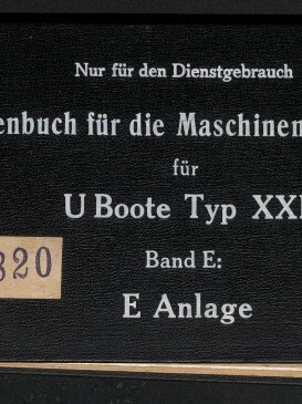 Schwarzer, querformatiger Deckel eines gebundenen Skizzenbuchs mit weißer Serifenschrift, oben die Aufschrift Nur für den Dienstgebrauch und Hauptausfertigung IV, mittig der Titel Skizzenbuch für die Maschinenmannschaft für U‑Boote Typ XXI Band E: E Anlage, links ein beigefarbenes Etikett mit der Signatur IV D 73–4820, eine Metallniete an der linken Kante und links unten das Logo des Internationalen Maritimen Museums Hamburg.