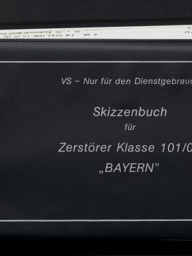 Schwarzes Skizzenbuch mit weißem Rahmen und aufgedrucktem Text VS – Nur für den Dienstgebrauch; Skizzenbuch für Zerstörer Klasse 101/03 „BAYERN“; links unten Museum-Logo und Schriftzug Internationales Maritimes Museum Hamburg; obere Kante zeigt eingeschobene Seiten.