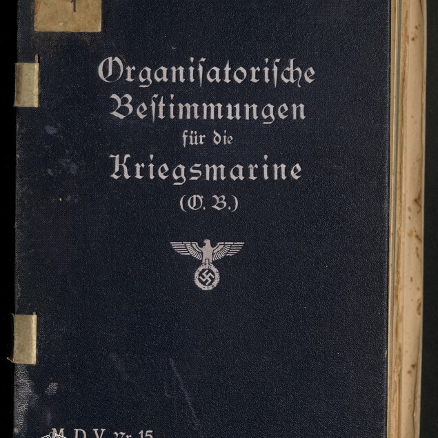 Dunkelblauer Einband eines Buchs mit weißer Frakturaufschrift „Organisatorische Bestimmungen für die Kriegsmarine (O.B.)“, darunter ein Reichsadler mit Hakenkreuz und unten links das Logo des Internationalen Maritimen Museums Hamburg.