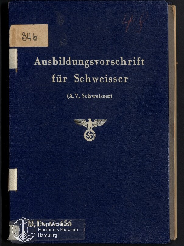 Blaue Buchdeckel eines Lehrbuchs mit weißer Prägung „Ausbildungsvorschrift für Schweisser (A.V. Schweisser)“ und einem Reichsadler mit Hakenkreuz, oben links ein Papieraufkleber mit der Zahl 346 und unten links das Logo des Internationalen Maritimen Museums Hamburg.