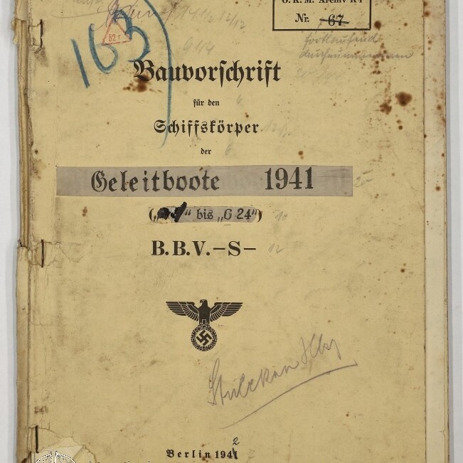 Vergilbtes, fleckiges Deckblatt eines gebundenen technischen Hefts von 1941 mit dem Titel „Bauvorschrift für den Schiffskörper der Geleitboote“, handschriftlichen Anmerkungen, Nummernstempeln und dem Reichsadler mit Hakenkreuz, sichtbaren Knicken und abgesplittertem Buchrücken.