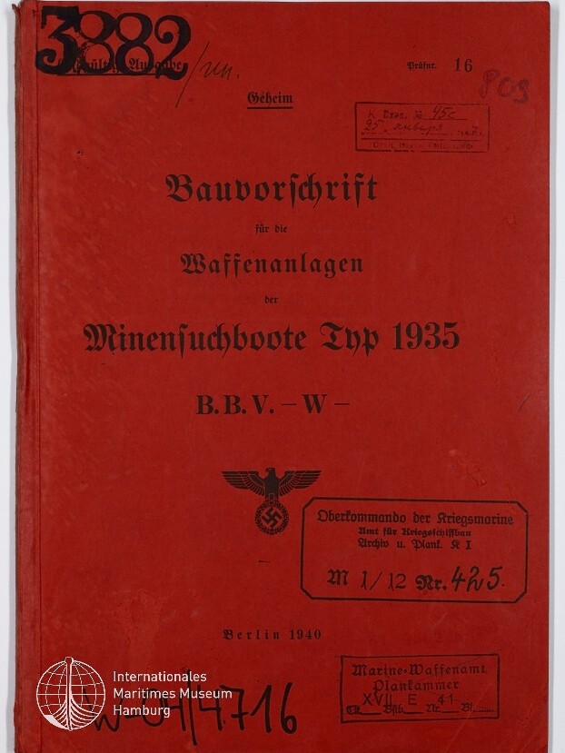 Rotes Deckblatt eines 1940 in Berlin erschienenen Dokuments mit dem Titel Bauvorschrift für die Waffenanlagen der Minensuchboote Typ 1935 in schwarzer Frakturschrift, versehen mit NS-Adler und Hakenkreuzstempel, mehreren Dienststempeln, handschriftlichen Nummern und dem Logo des Internationalen Maritimen Museums Hamburg unten links.